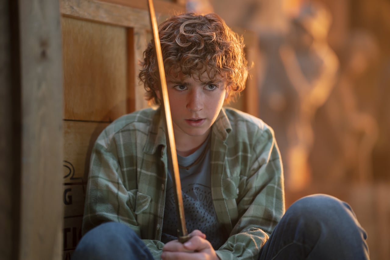 A young teen is crouched with a sword in his hand. 