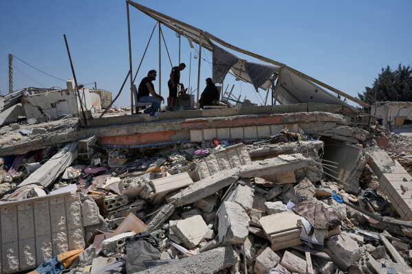 A Lebanese family take shade under damaged solar panels of their destroyed house in the village of Zawtar al-Gharbieh, south Lebanon, Wednesday, Aug. 5, 2026. (AP Photo/Mohammed Zaatari)