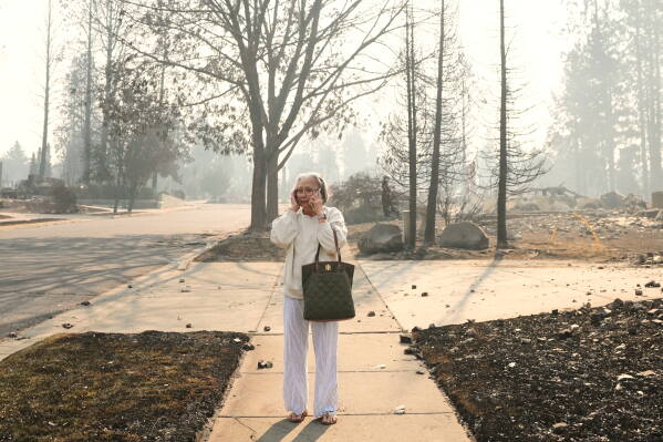 Miriam Sim, 76, reacts as she walks through the burned remains of her neighborhood after a wildfire hit the northern part of Spokane, Wash., Monday, Aug. 3, 2026. (AP Photo/Lindsey Wasson)