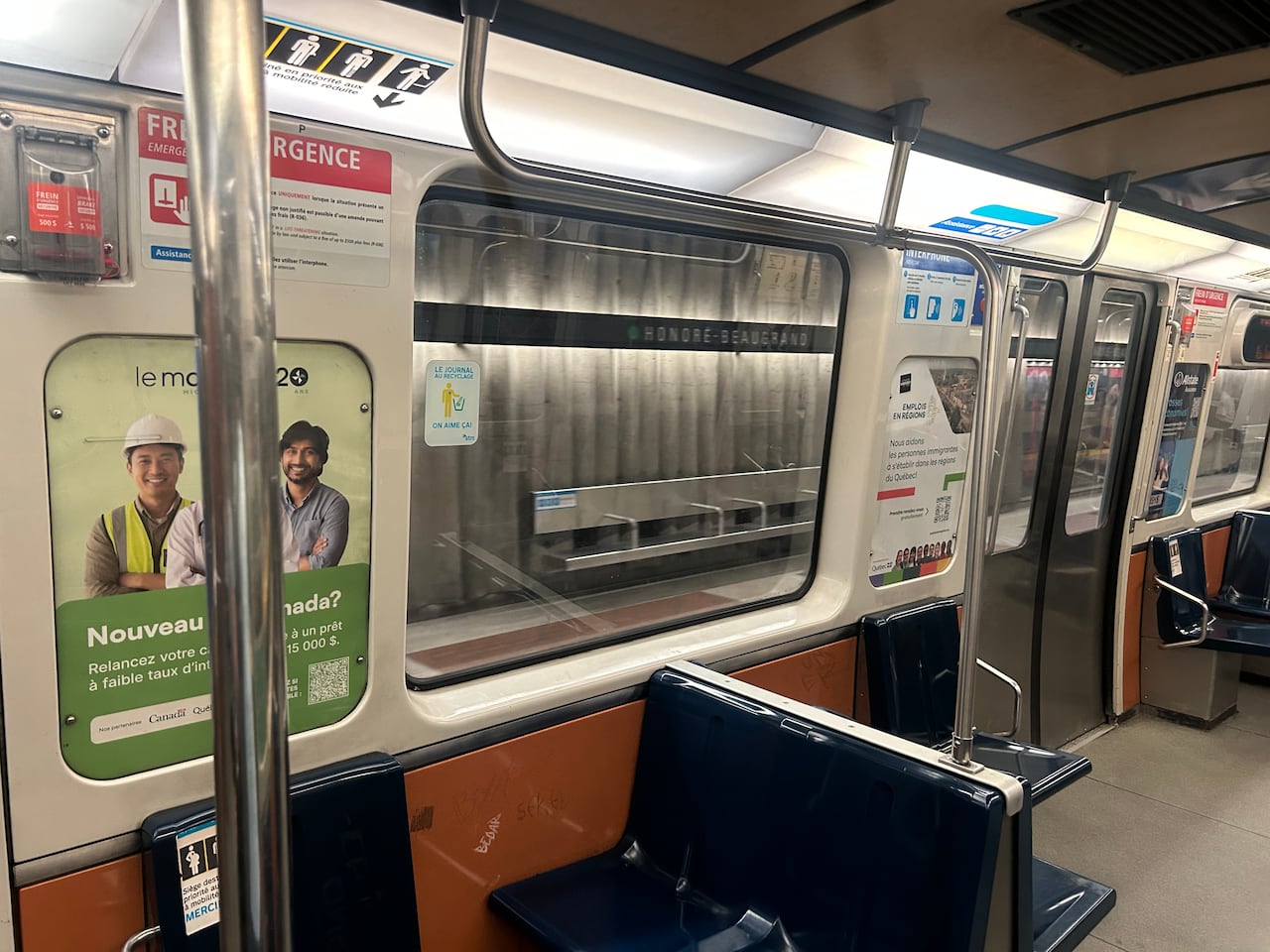 The interior of a montreal metro car, a blue hard plastic seat appears behind a floor to ceiling metal pole.