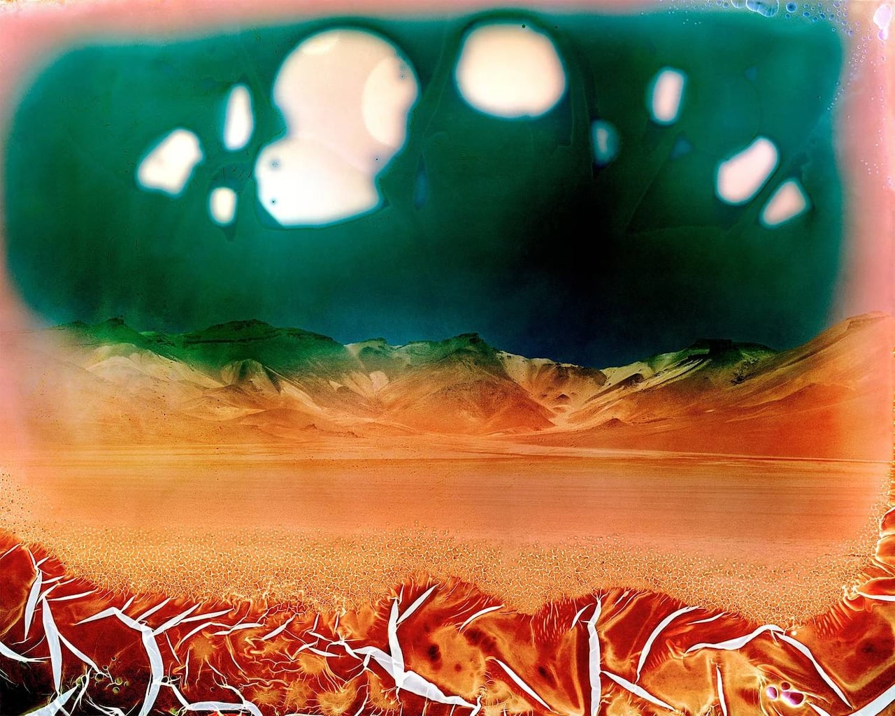 Psychedelic style altered photo of a desert landscape. Washes of acidic green, red and orange saturate the image.