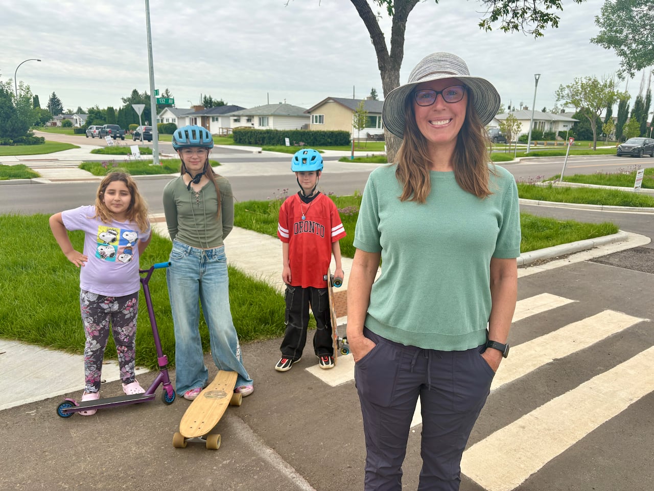 A woman in a sunhat with three kids on scooters and skateboards behind her.