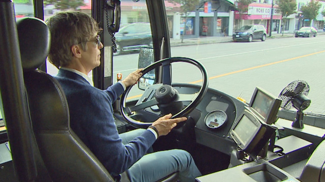 A woman with short hair wearing blue drives a bus.
