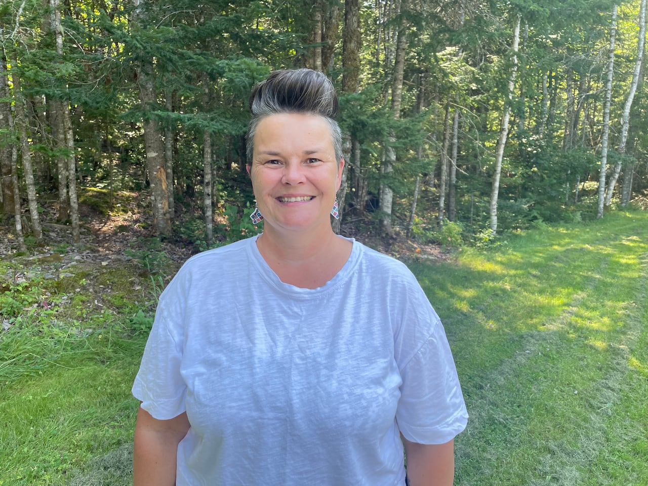 A woman with short grey hair wearing a white t-shirt.