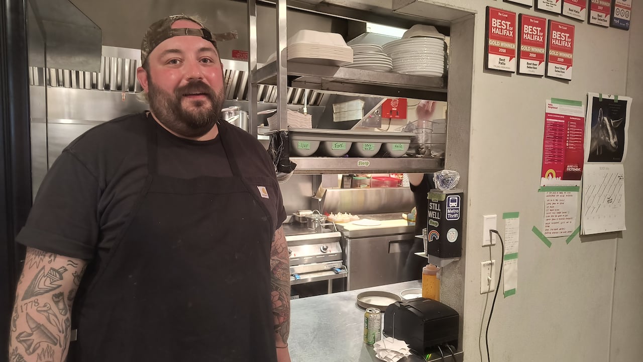 A chef with a very red face next to the pass in a kitchen