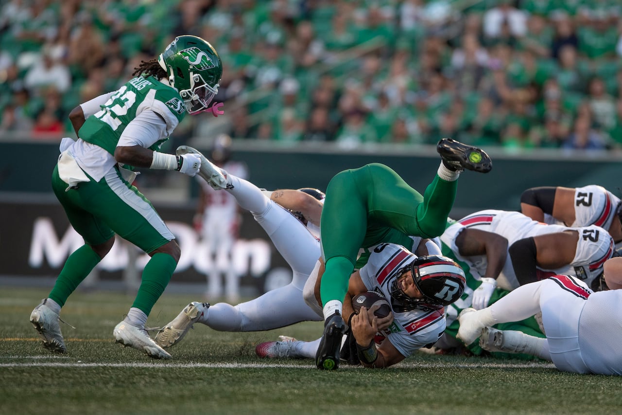 Ottawa Redblacks quarterback Bryson Barnes (bottom) scores a touchdown against the Saskatchewan Roughriders. Riders are stacked ontop of the player in a tackle.