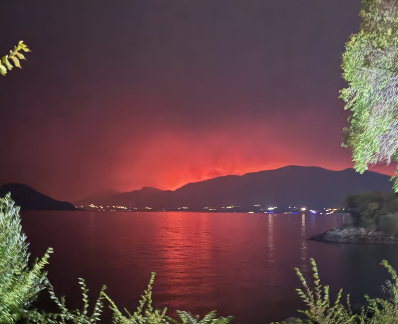Plumes of orange smoke are seen on hills across a lake.