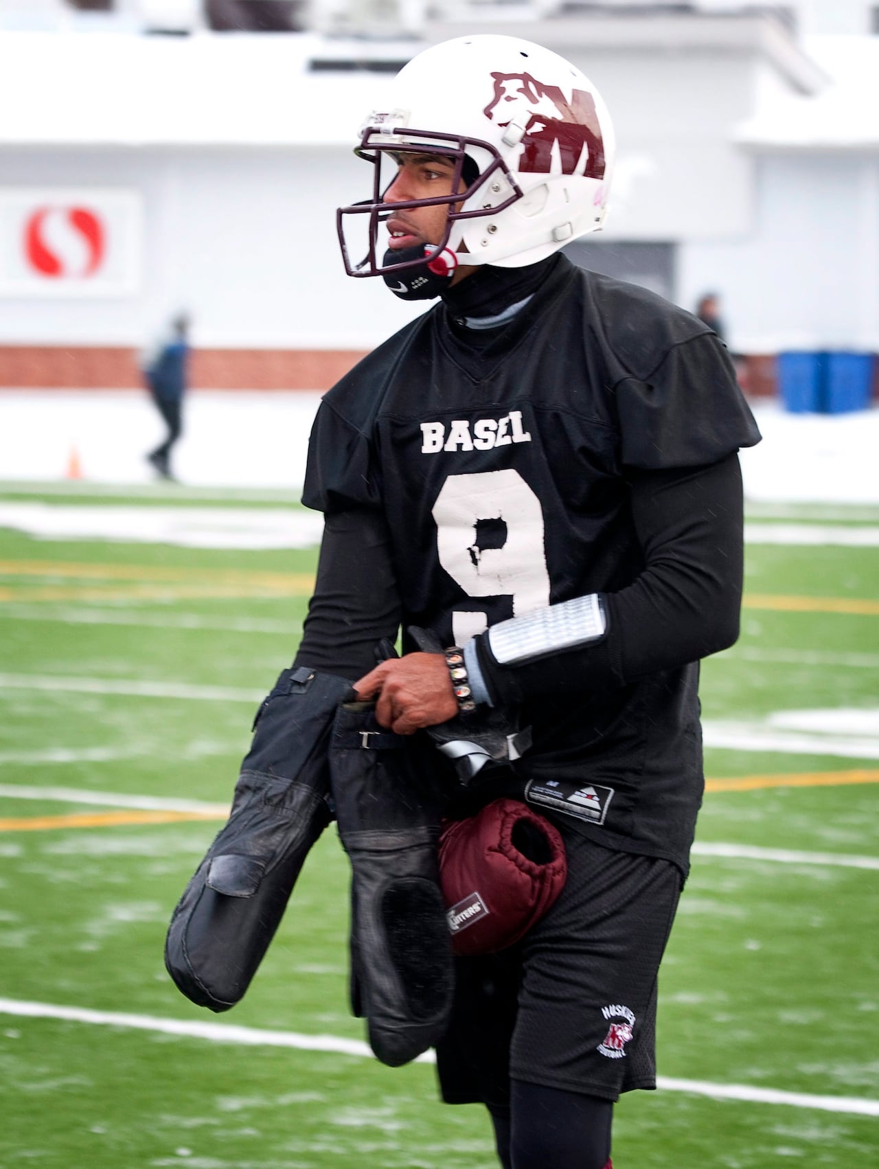 A football player wearing a maroon and white jersey is shown putting on snowmobiling gloves to keep his hands warm.