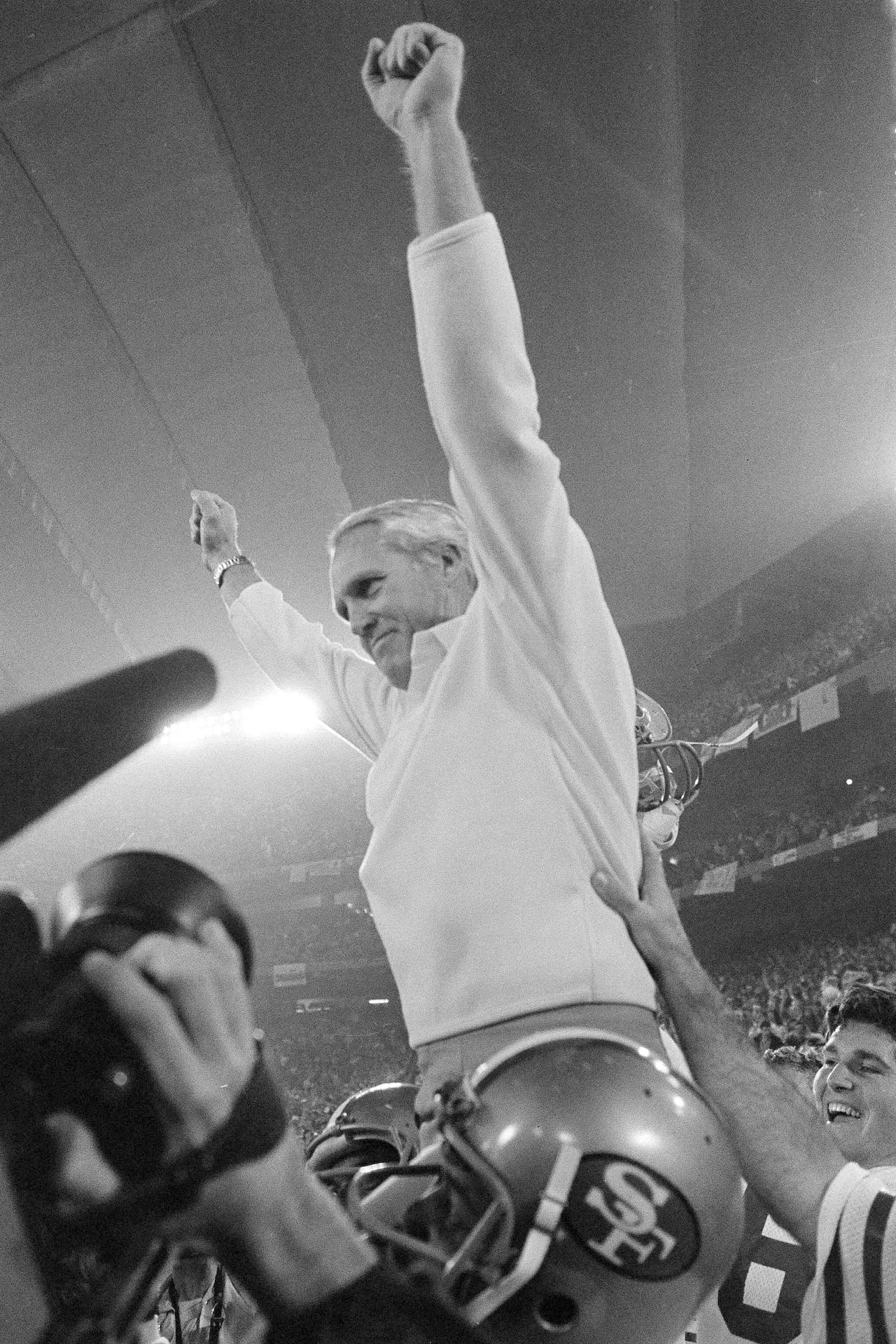 A black-and-white photo shows a coach being carried off the field by his players.