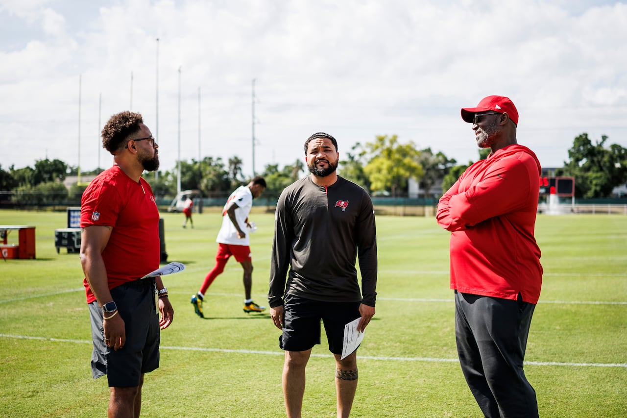 Three Black football coaches are shown on a field together.