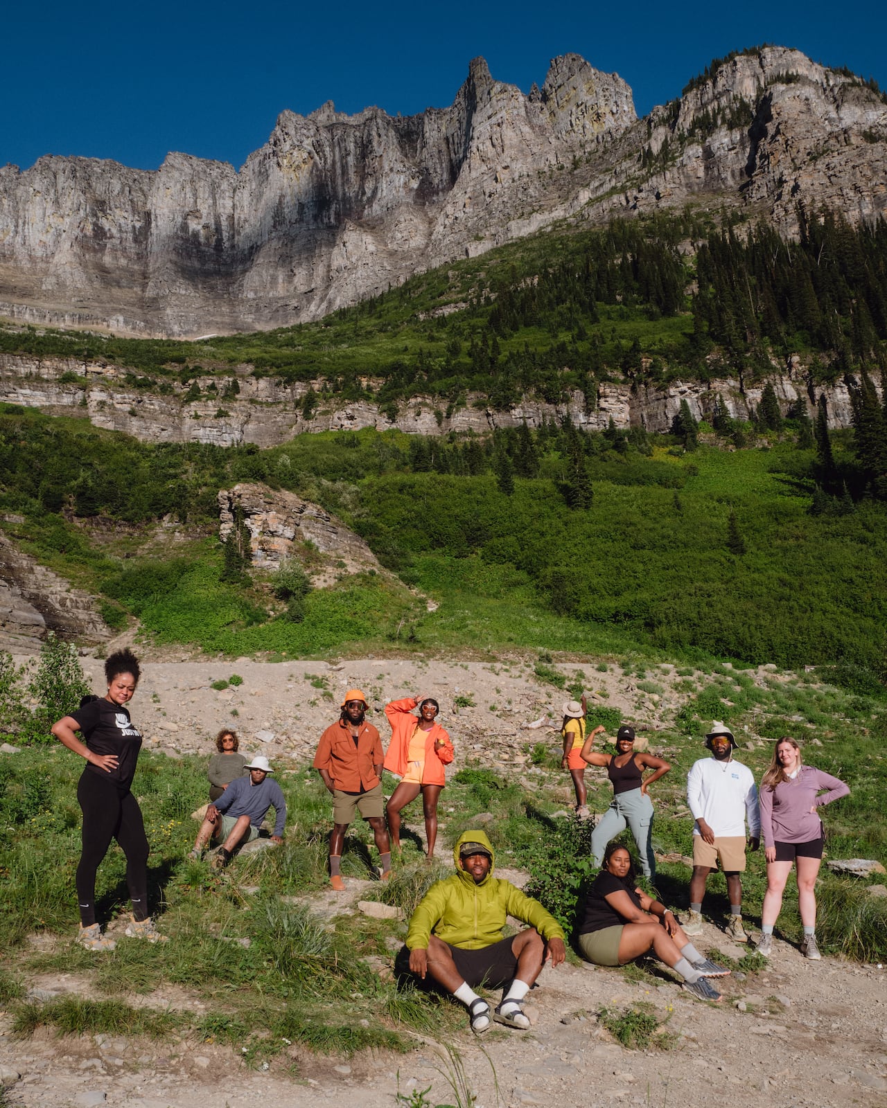 Group of campers standing and sitting in front of mountain.
