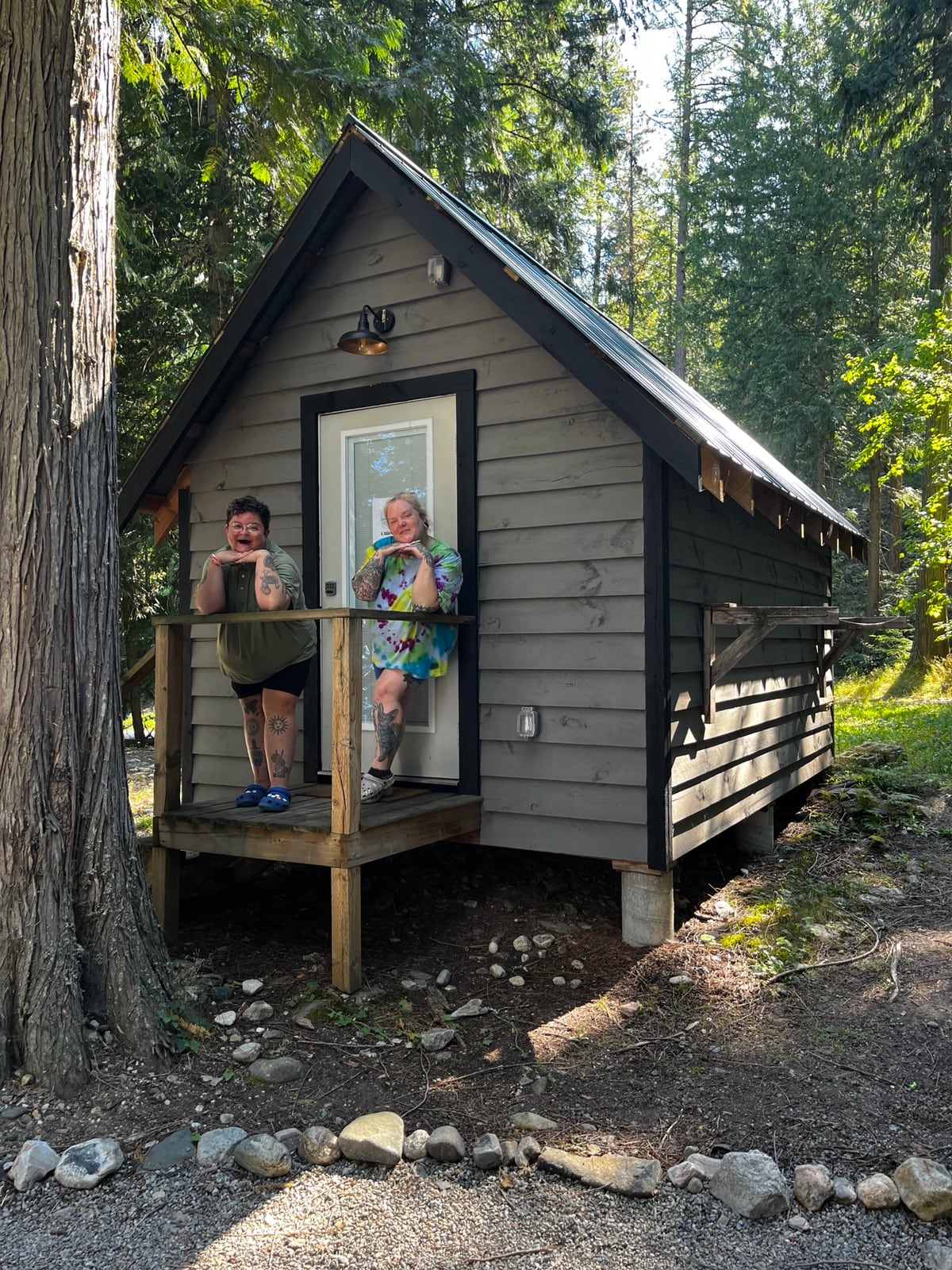 Two people posing with their hands resting under their chins pose standing by the entrance of a cabin