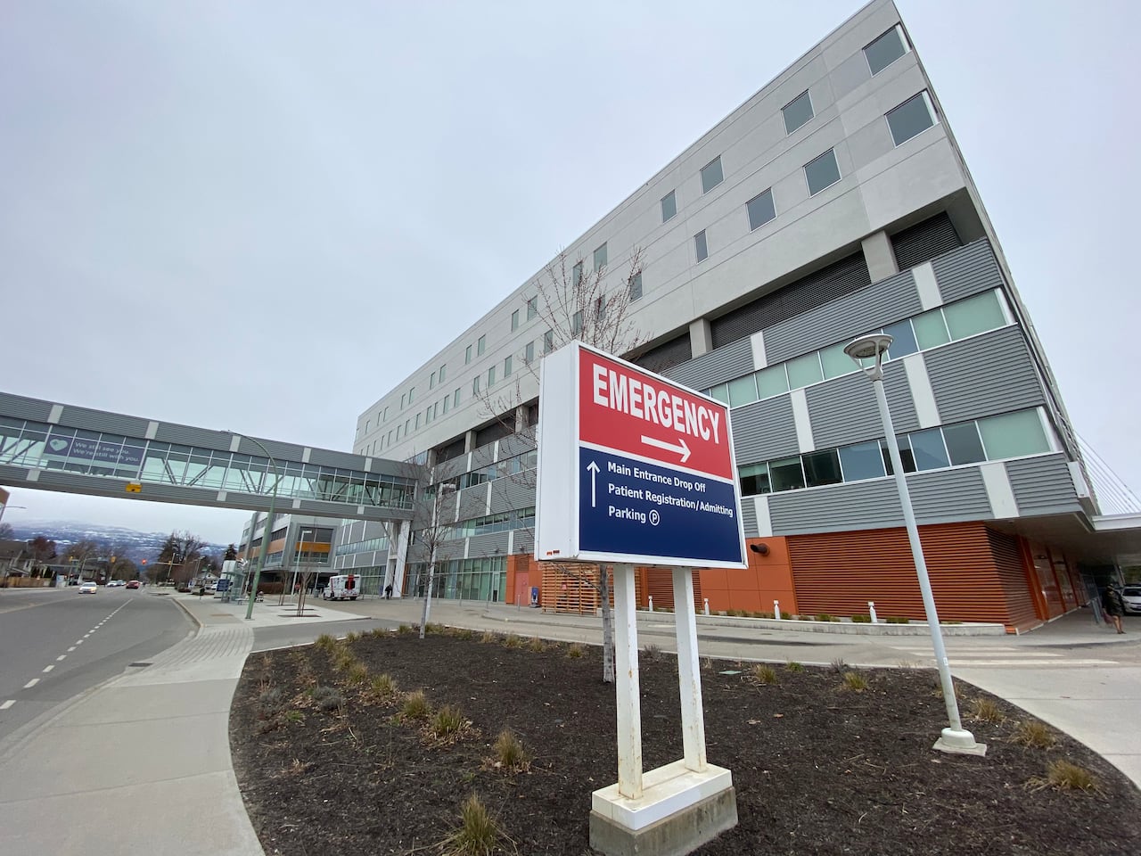 A wide-lens photo of the outside of a hospital, with a red sign reading 'Emergency.'