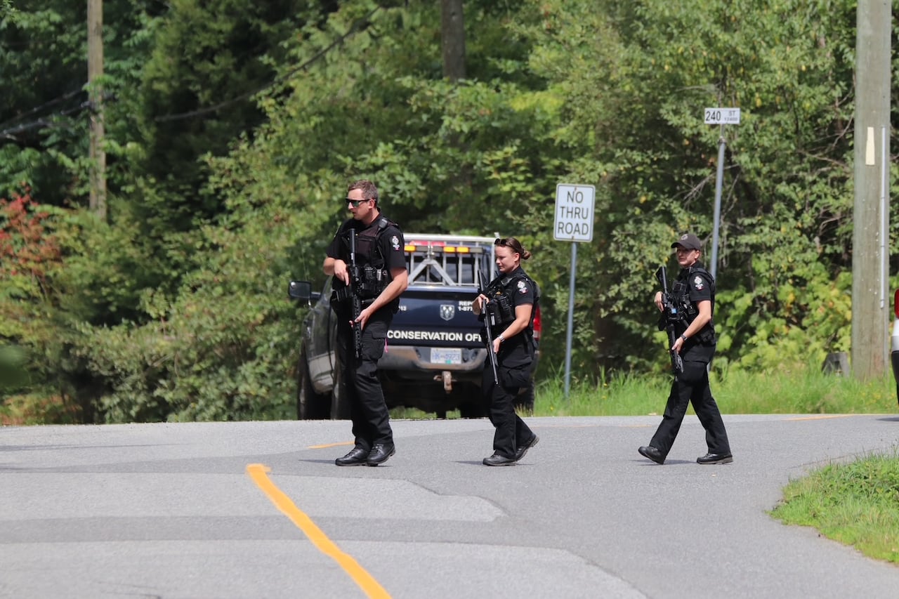 Three police officers with long guns walk in front of a conservation officer pickup truck