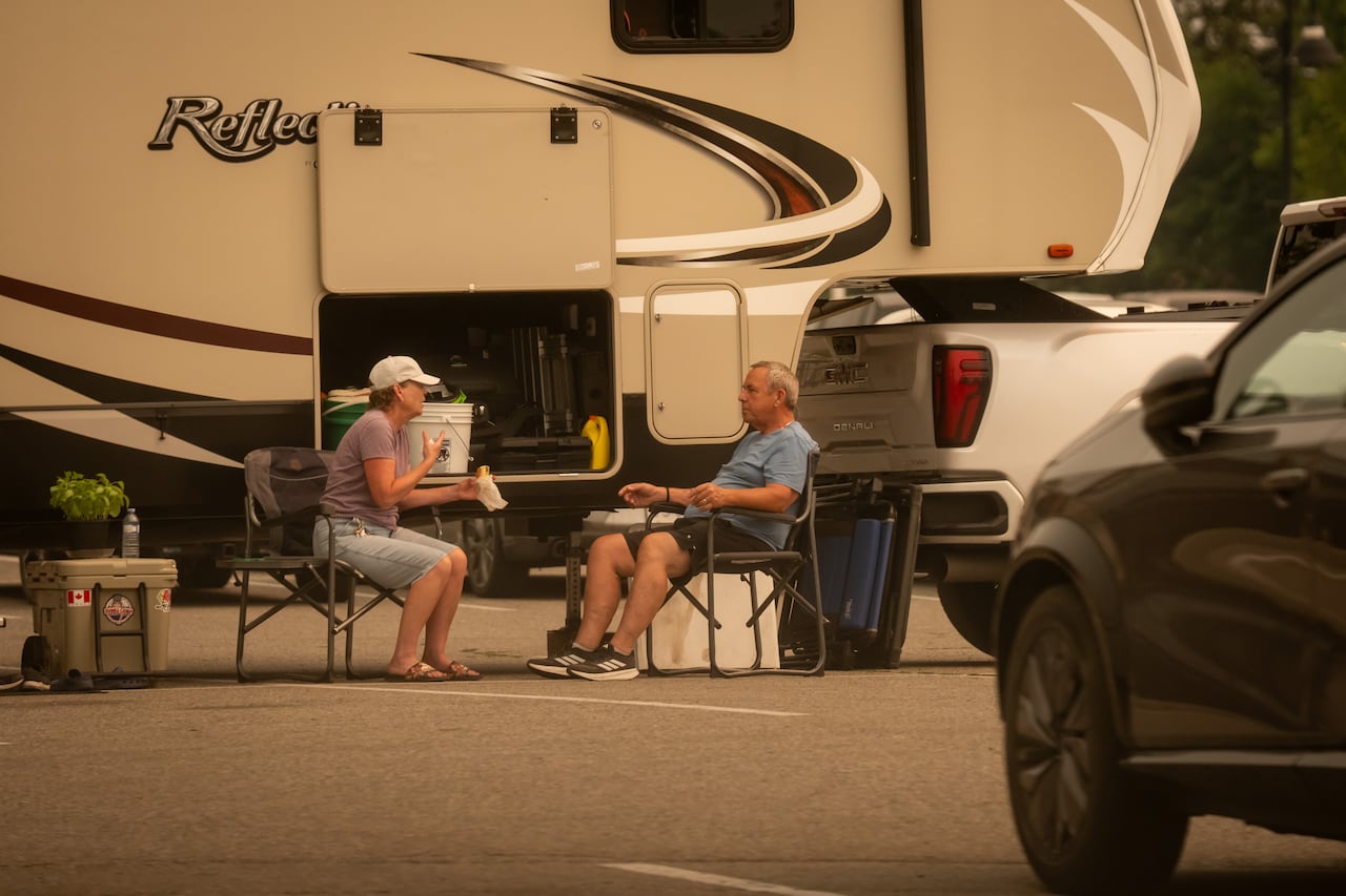 A woman and man are pictured with an amber haze across the scene, in camping chairs on the pavement.