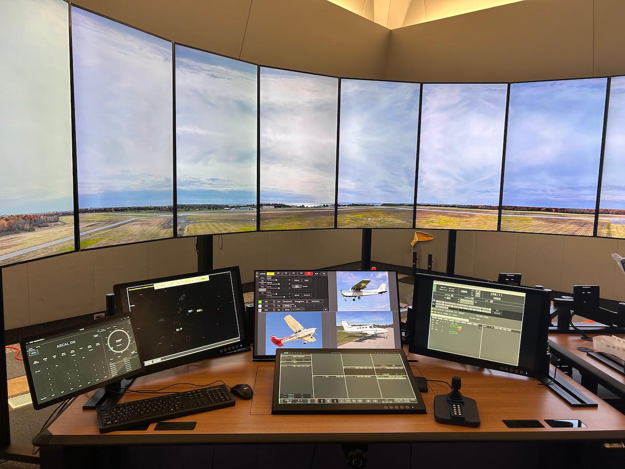 Twelve vertical monitors show parts of a single image in front of a desk with other monitors showing airplanes.