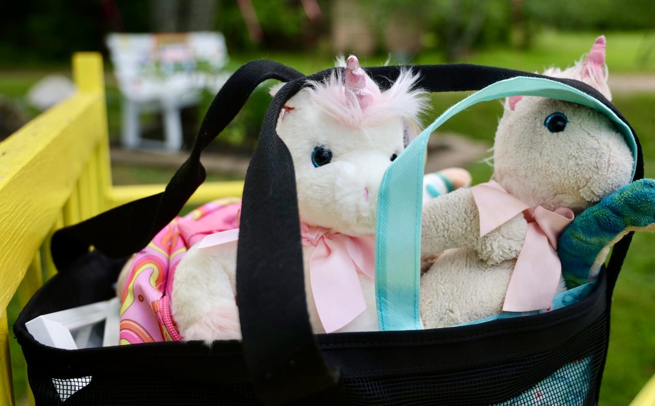 A brand new white unicorn stuffed animal sits next to the same stuffed animal but older in a black bag.