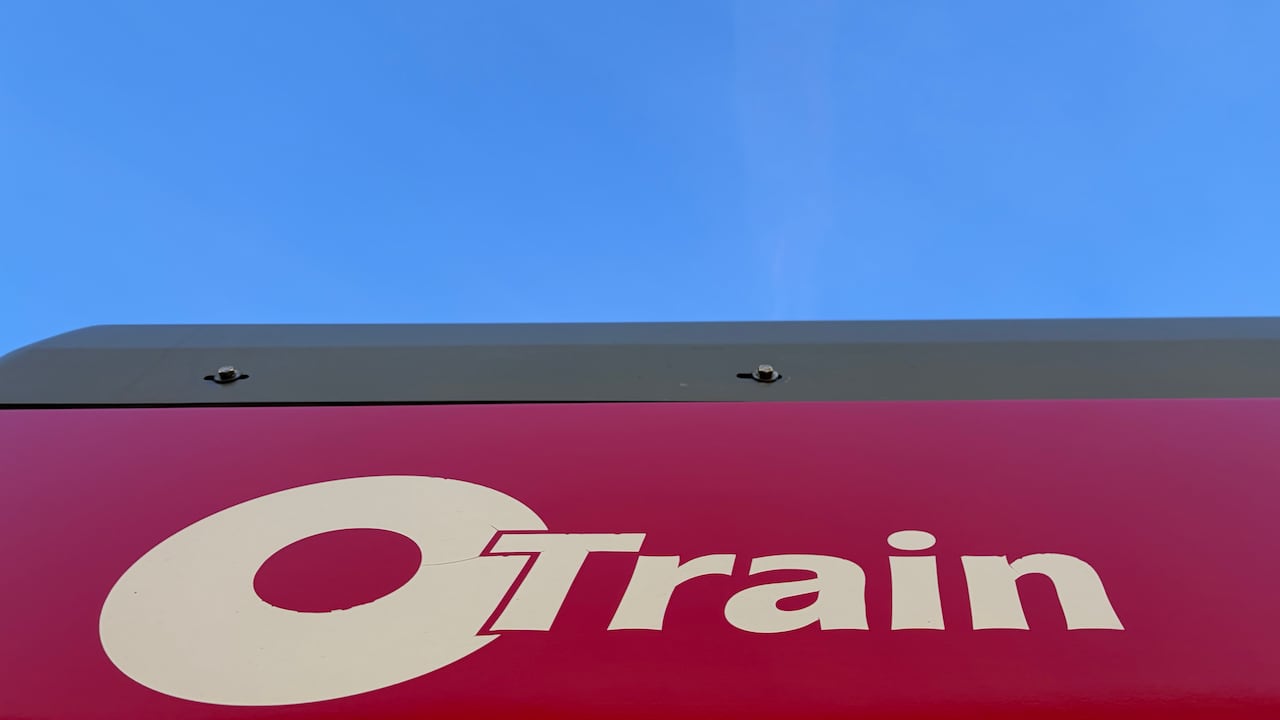 An O-Train logo on the side of a train on a sunny morning.