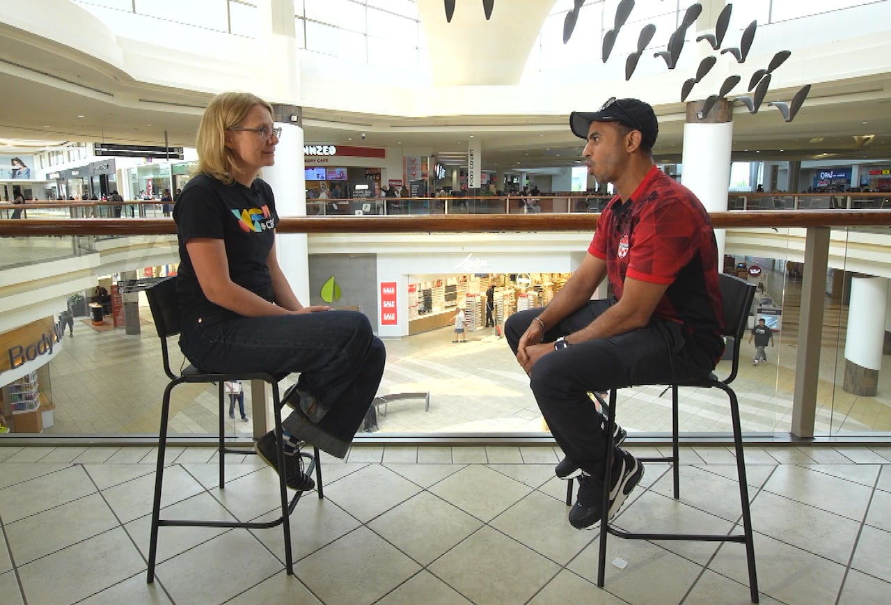 Two people sit on chairs facing each other in the middle of a mall.