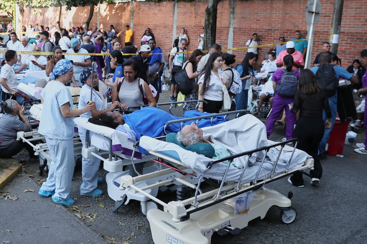 Several people are shown standing outside, with some in medical scrubs and others patients lying in beds.