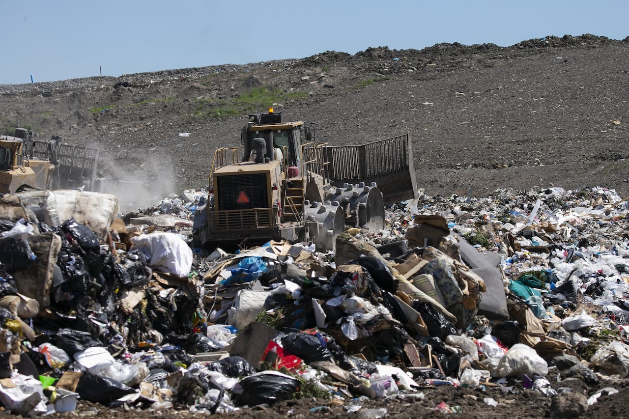 A waste compactor rolls over a huge pile of household trash at a landfill.