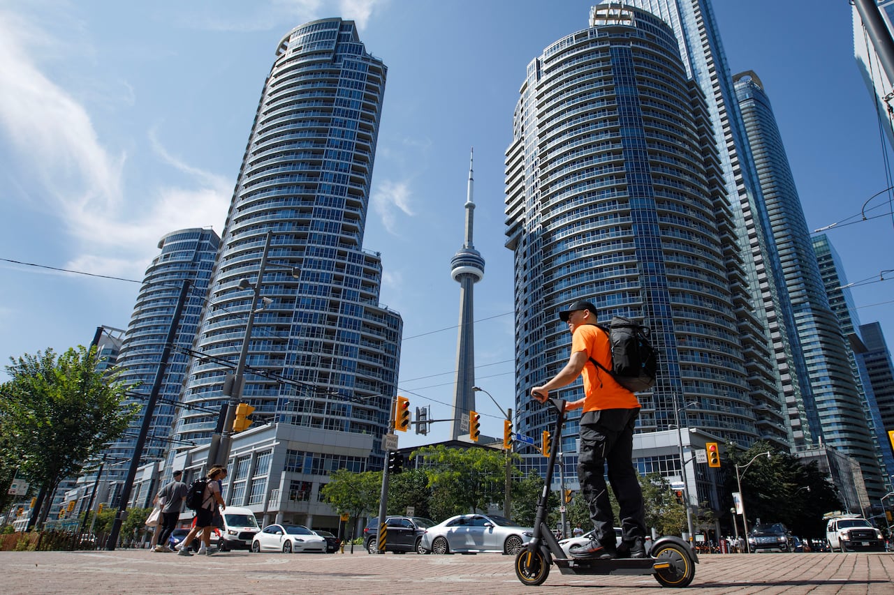 Person on e-scooter in front of CN Tower and other tall buildings