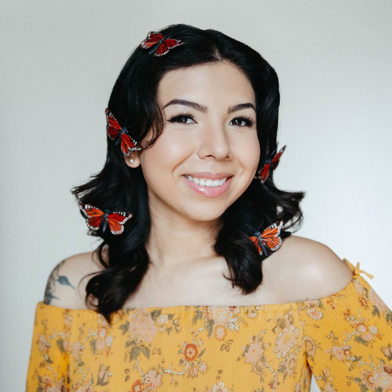 A smiling woman in a yellow top with butterfly pins in her hair.
