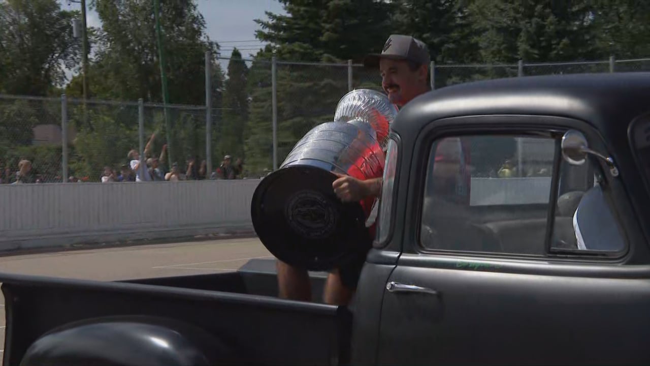 A man sits in the back of a pick-up truck, holding a large award.