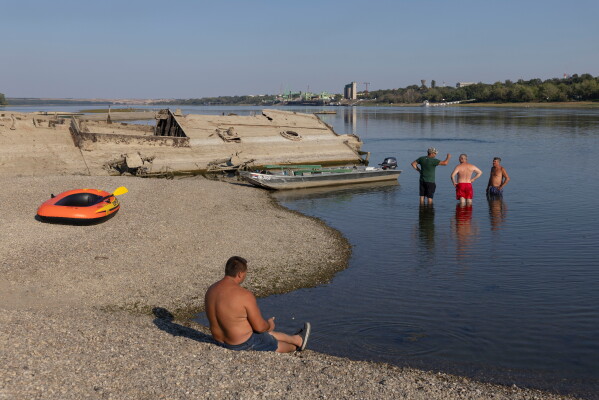 Curious onlookers gather near the wreckage of a WWII German warship that emerged due to low water levels in the Danube river near Prahovo, Serbia, Tuesday, Aug. 11, 2026. (AP Photo/Marko Drobnjakovic)