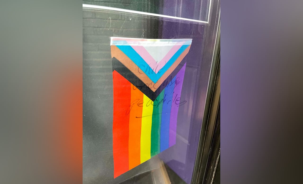 The phrase "child grooming pedophiles" is written on glass in front of a small Pride flag.