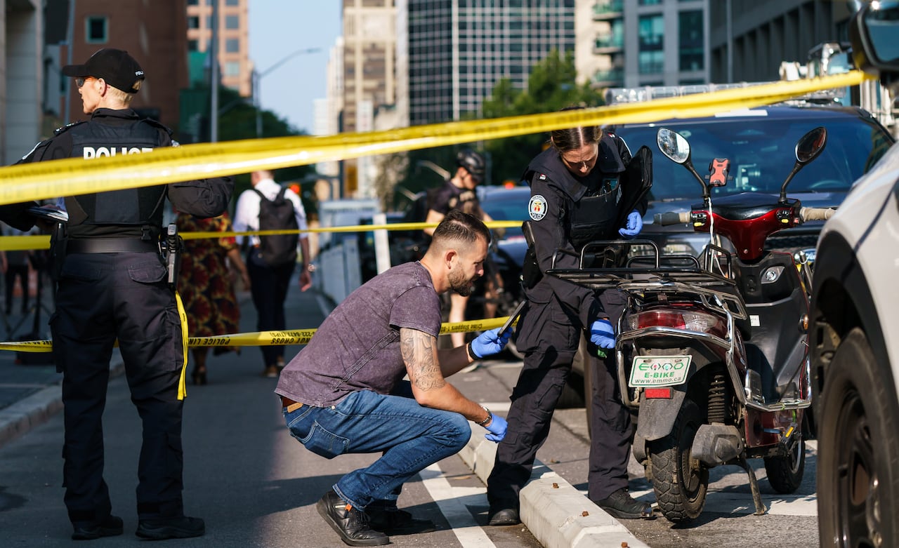 Man crouches while police investigate the shooting of an officer after an e-bike robbery.