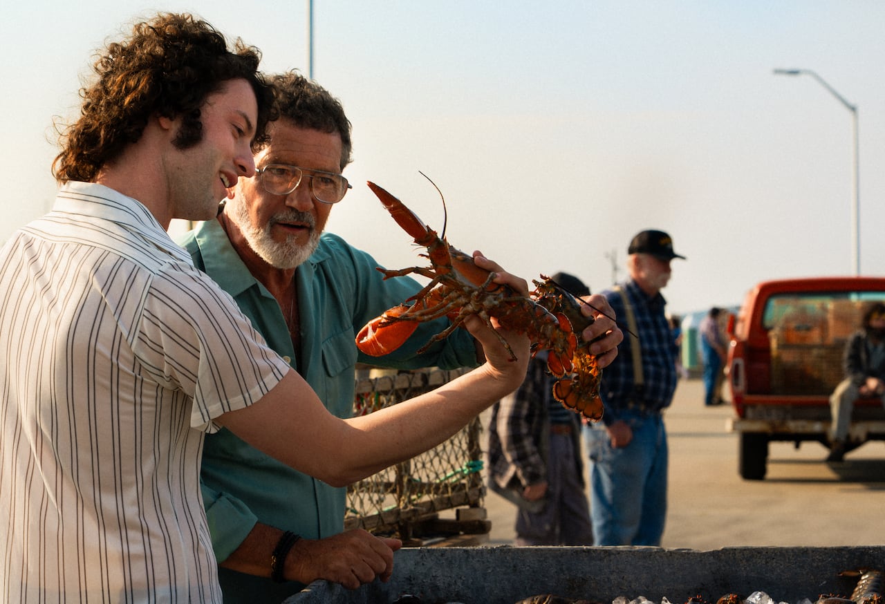 A young man in a white and black striped shirt and and older man with a beard and glasses hold a large lobster while standing in the street.