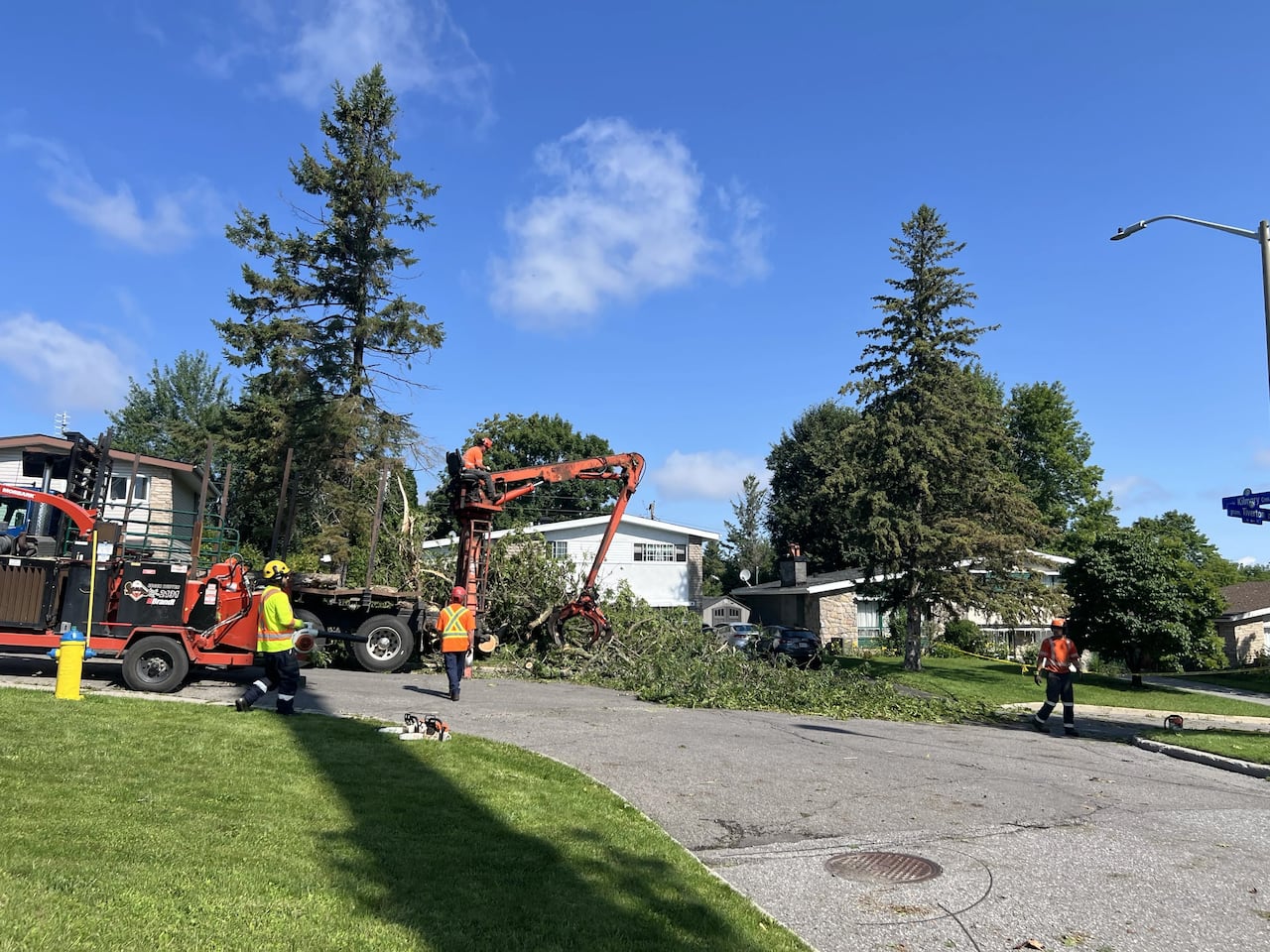 Workers and heavy equipment take away damaged trees from a residential area of a city.