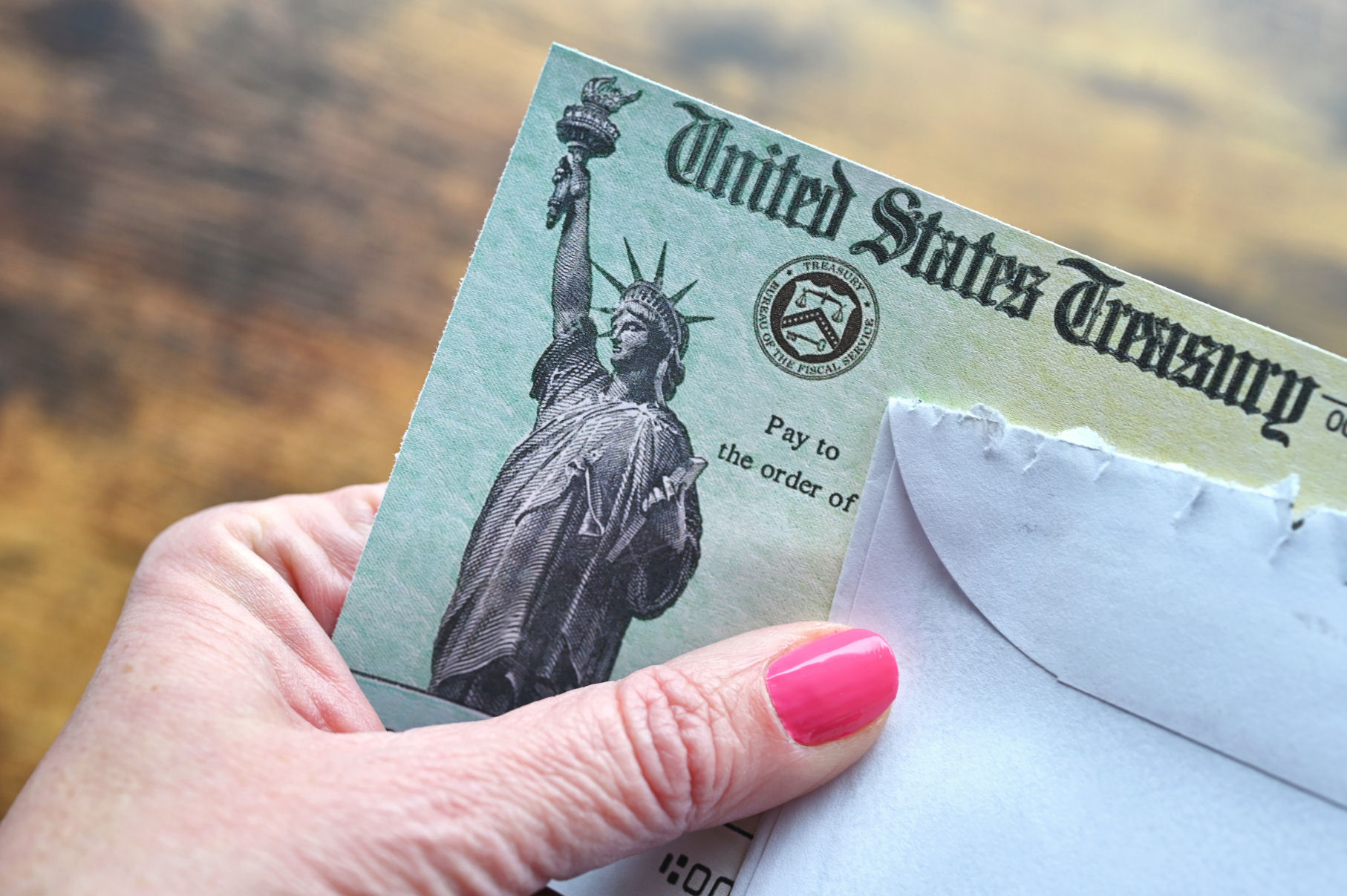 A hand is holding a Social Security check issued by the U.S. Treasury.