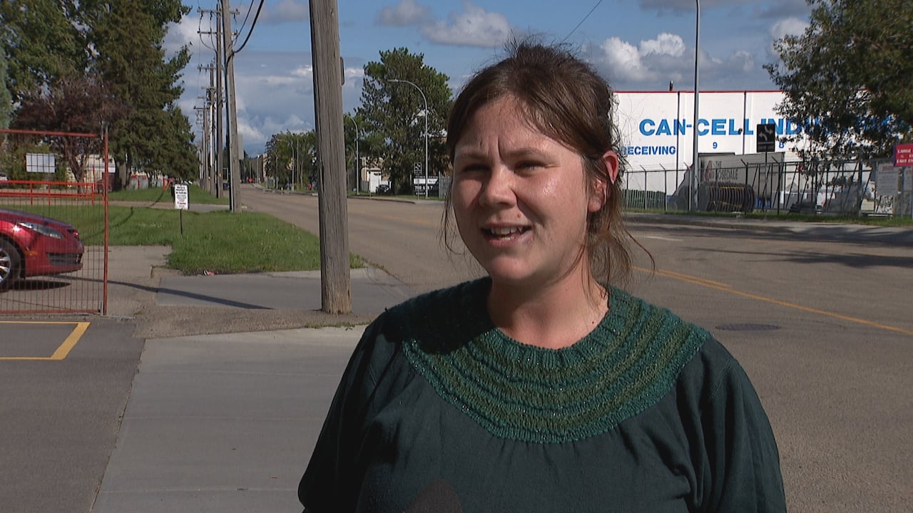 A woman in a green shirt stands on a street.