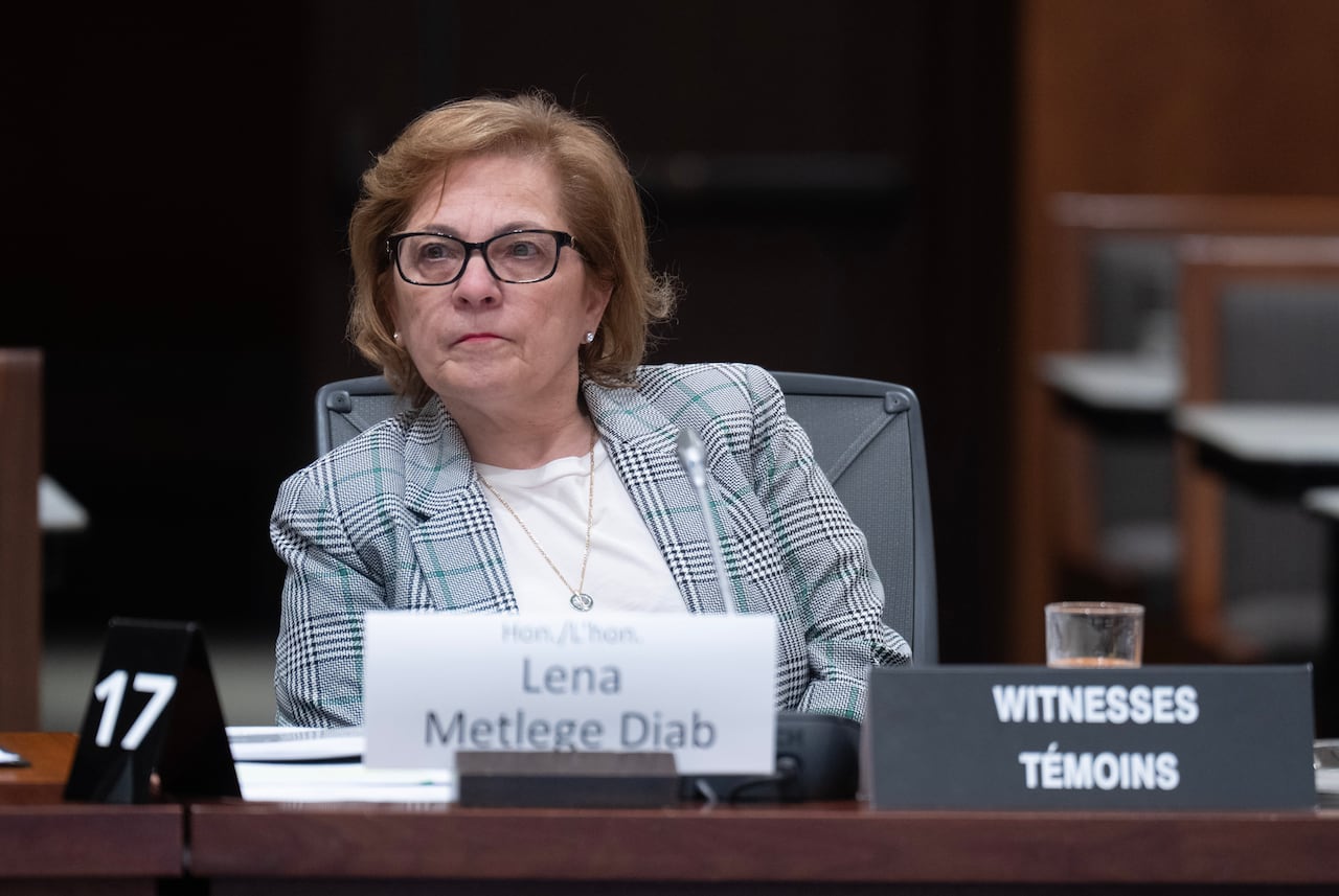 A woman in a blazer sits at a desk, with a nameplate in front of her.