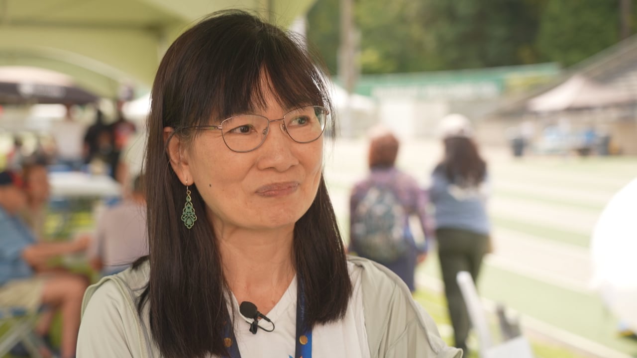 An East Asian woman smiles while at a running track.