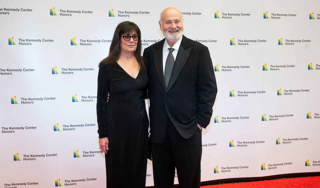 A man and a woman stand together on a red carpet, smiling.