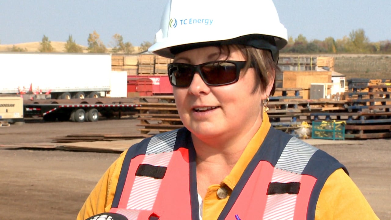 A woman wearing a hard hat stands in front of a construction laydown area.