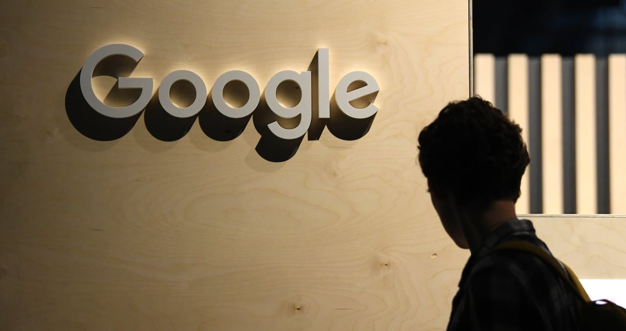 A person is in dark silhouette next to the three dimensional letters spelling out "Google" on a wall.