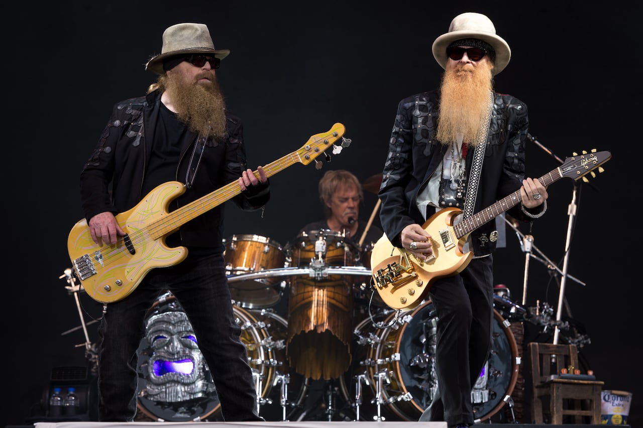 Two men with long beards play guitar in front of a guy playing drums
