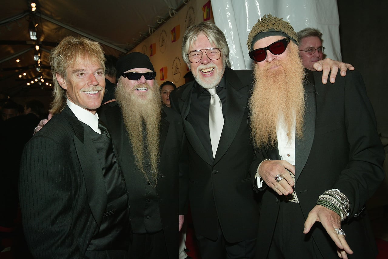 Four men dressed in dark clothes, two with long beards, smiling at the camera