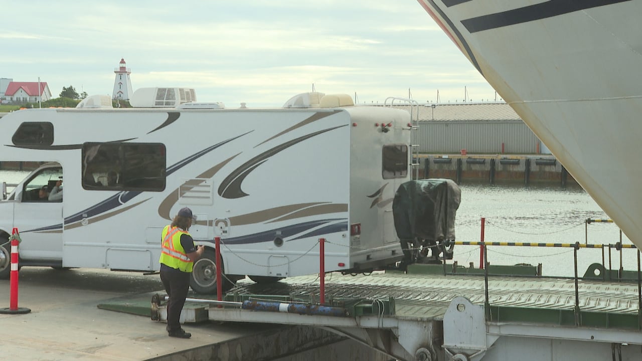 An RV is seen exiting a ferry while a person stands nearby.