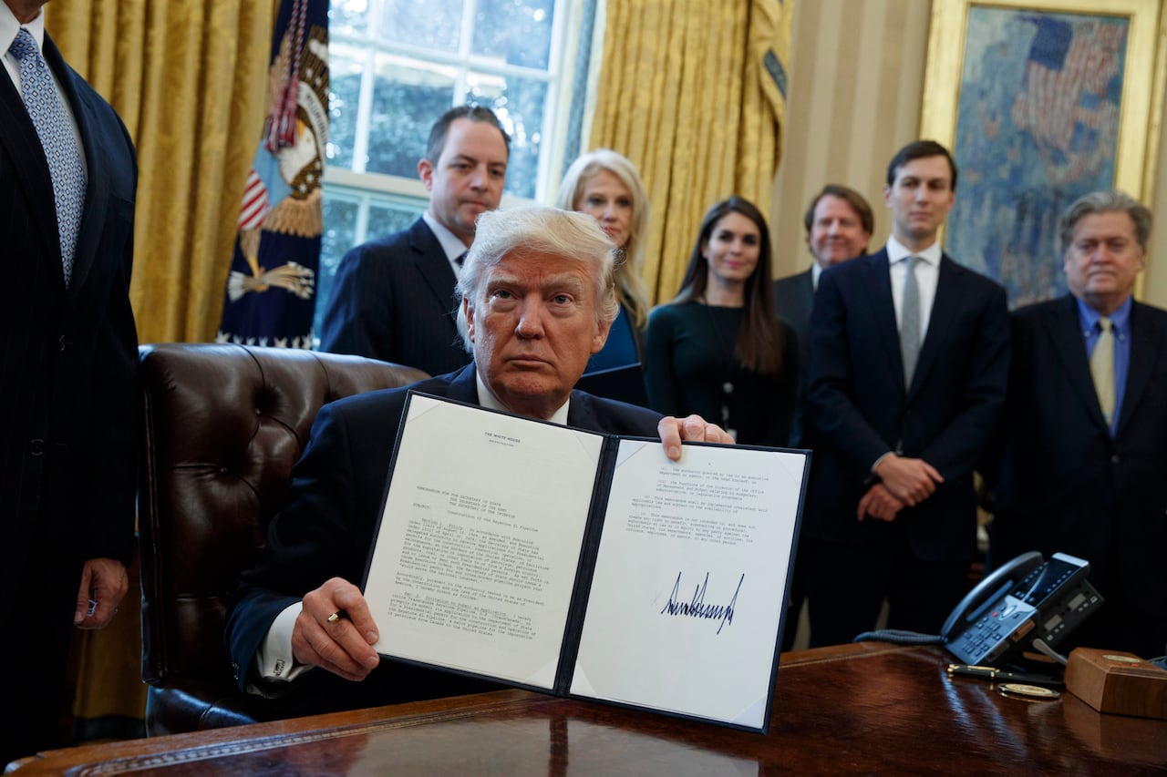 A man sitting at a desk holds up a document with a group of people standing behind him.