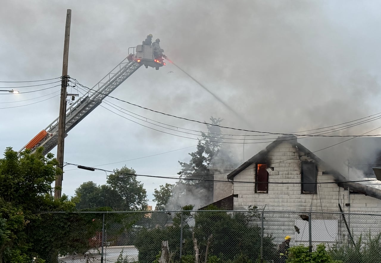 Firefighters on a ladder spray water onto a burning house