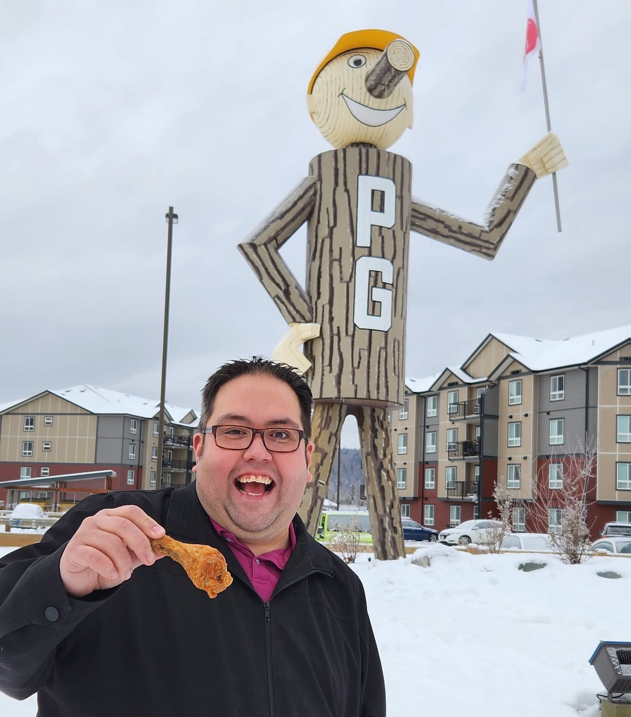 A man holding a fried chicken drumstick standing in front of a giant wood man.