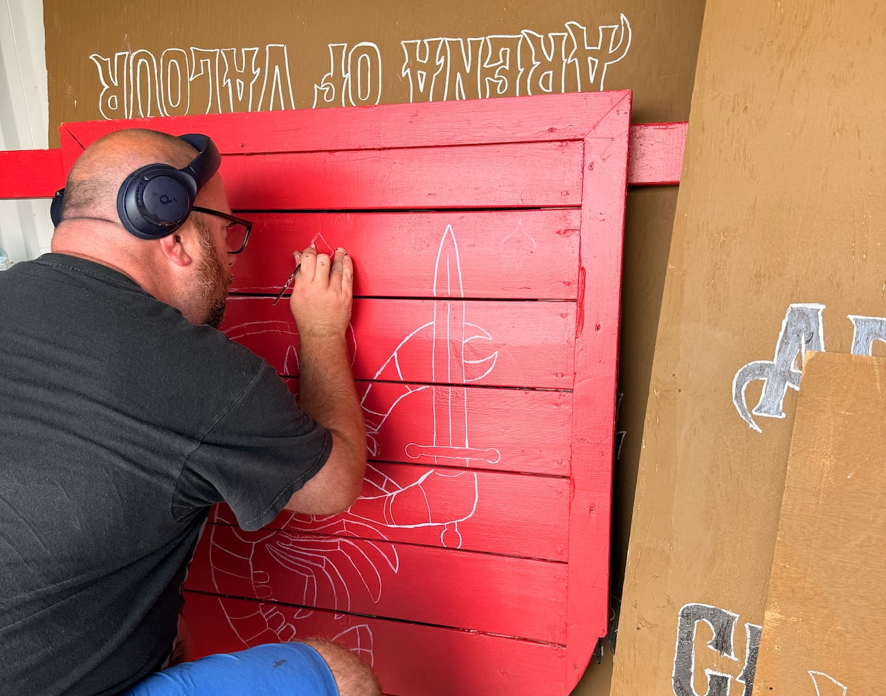 A man drawing on a red shield, while wearing over-the-ear headphones