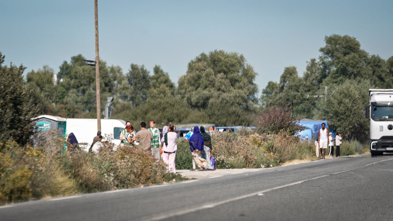 People are seen walking on the side of the road near tents.