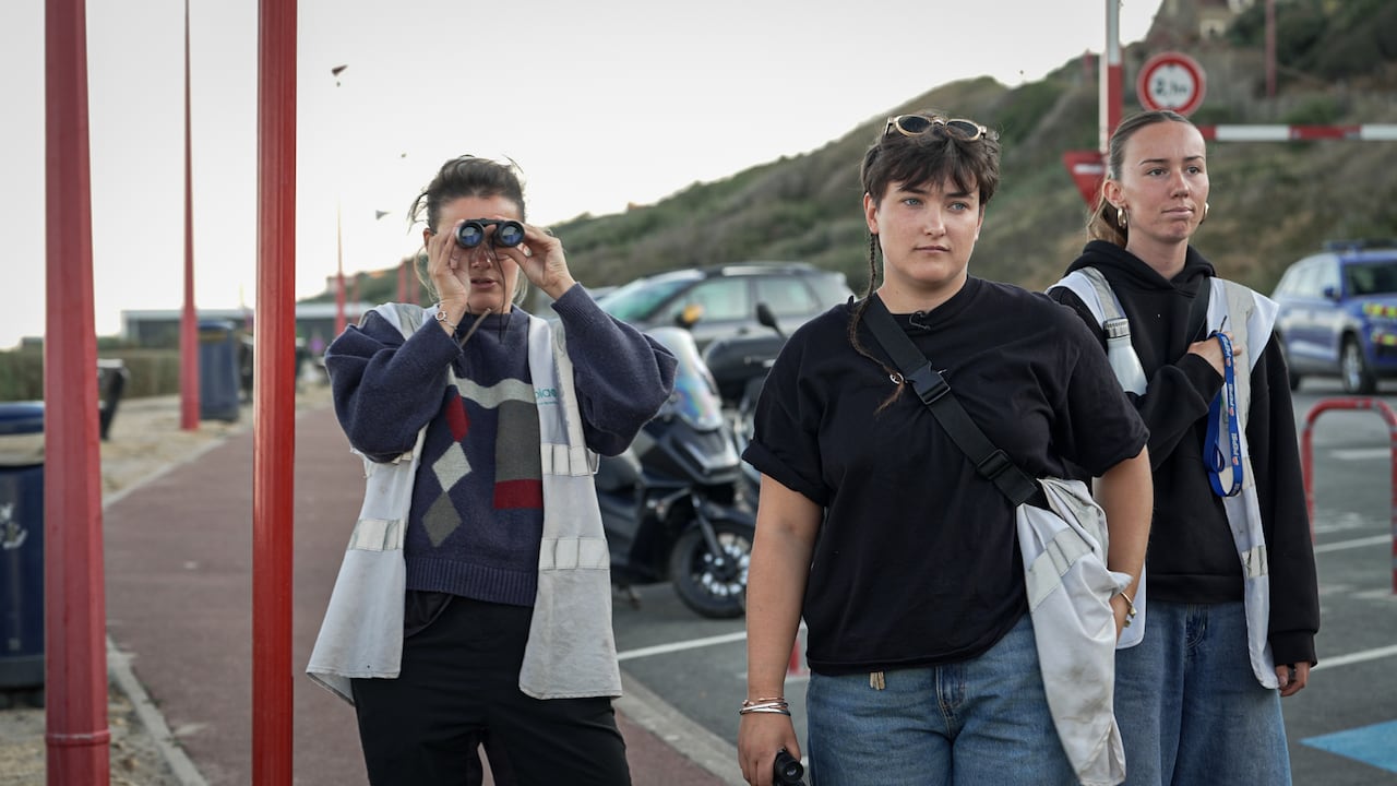 Three women are seen standing in a parking lot on a beach carrying binoculars.