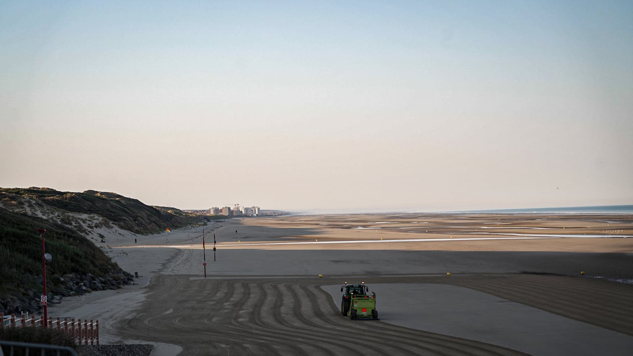 A beach is seen with dunes and a tractor flattening sand.